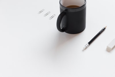 三个白色的回形针，黑色的陶瓷杯，黑色的铅笔，白色的铅笔擦在白色的表面